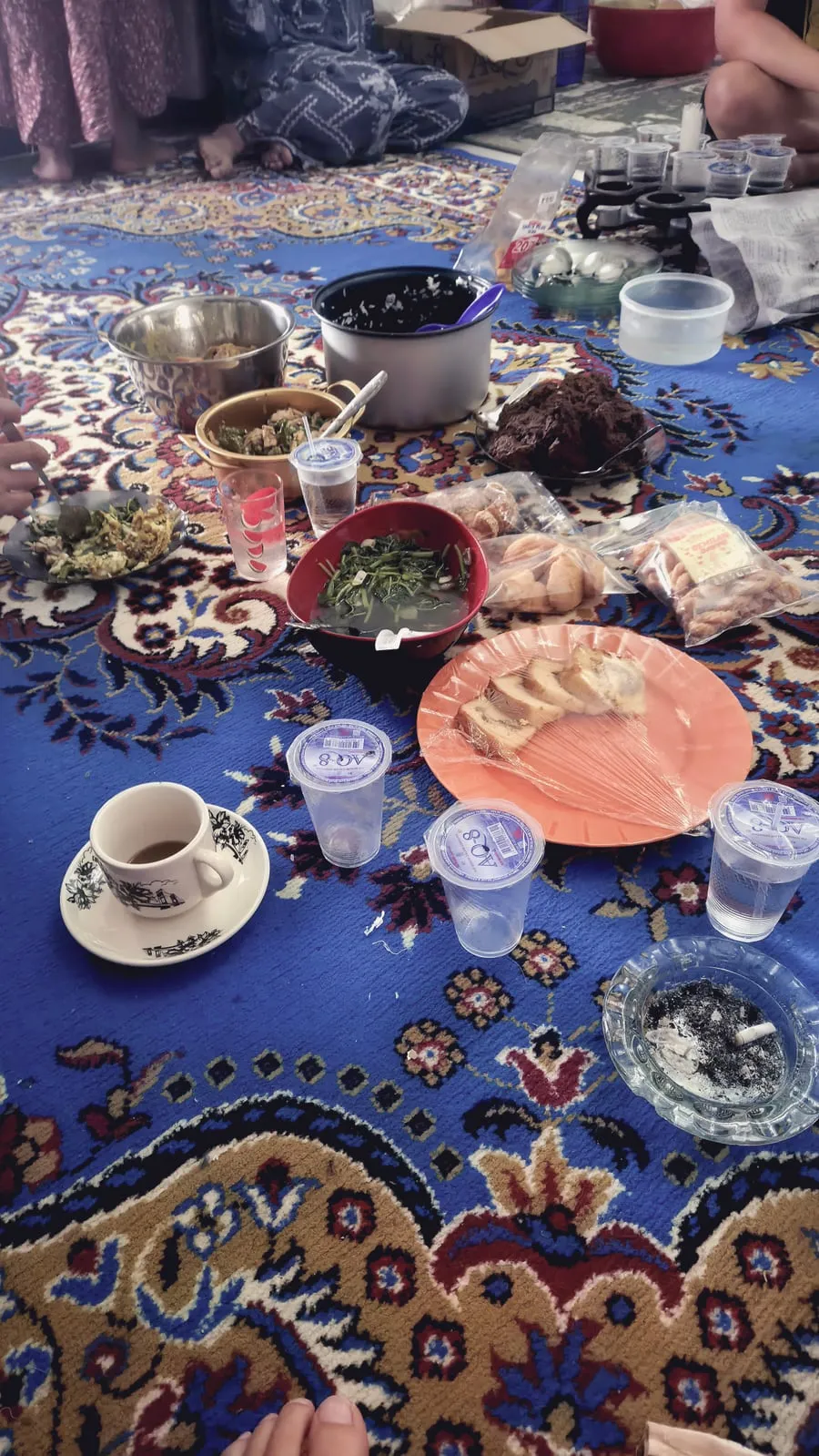 Hidangan di atas kain bermotif biru, dengan mangkuk kecil, kopi, dan gelas berisi es.