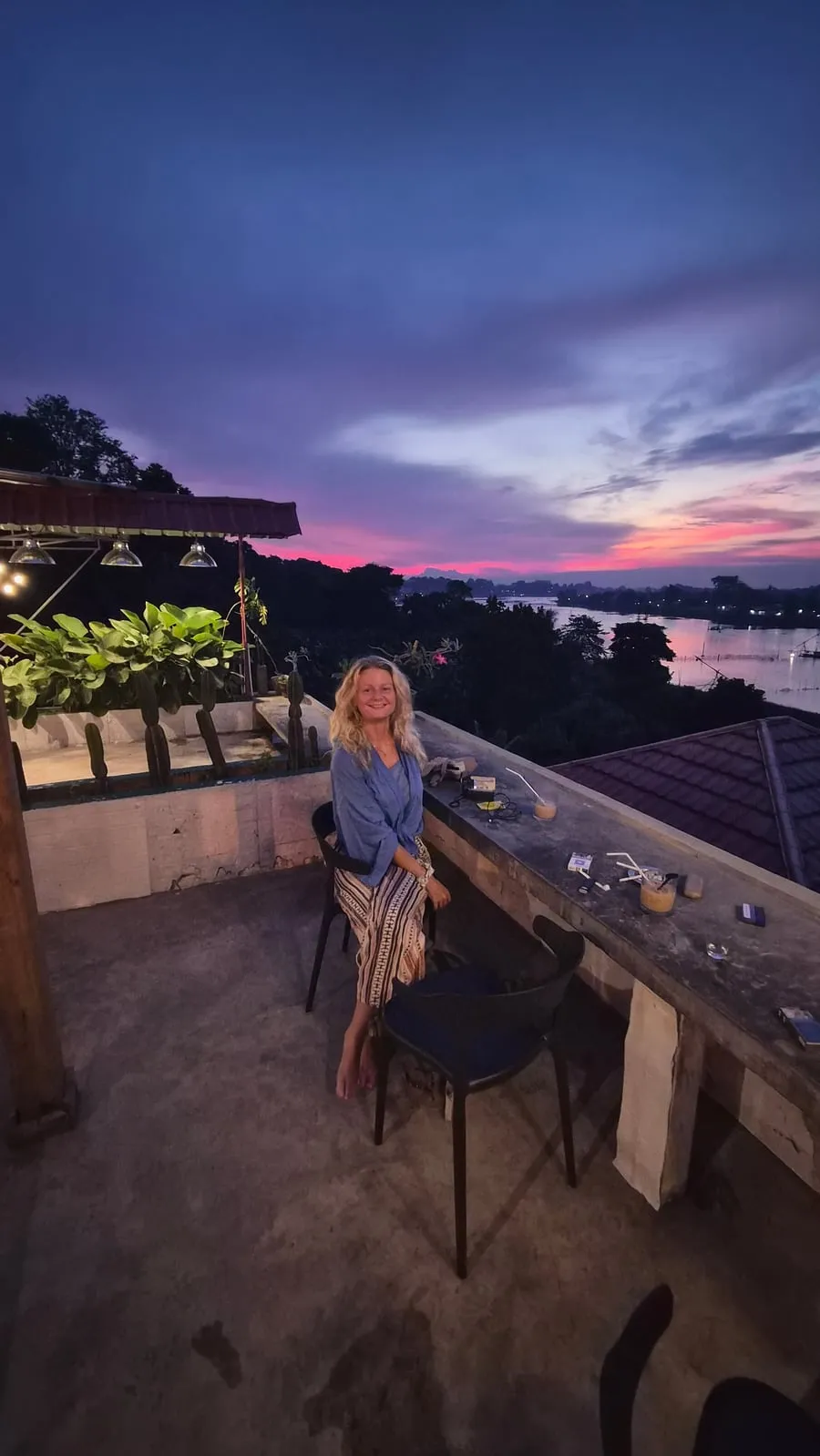 Tine berdiri di pagar atap memandang matahari terbenam berwarna merah muda dan oranye di atas laut.